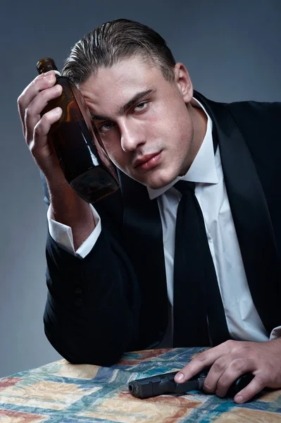 Depressiver junger Mann mit Flasche und schwarzer Waffe in der Hand — Stockfoto