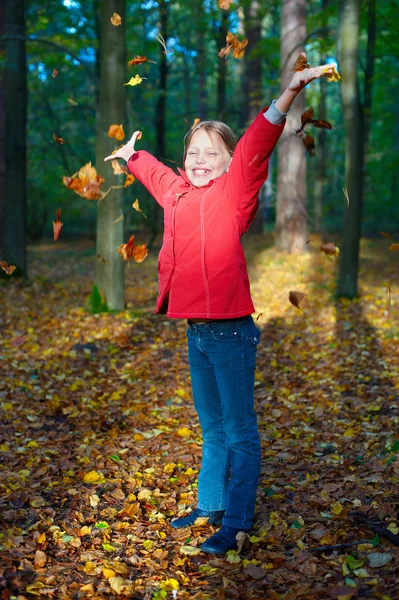 Привлекательный портрет улыбающейся маленькой девочки, бросающей листья — стоковое фото