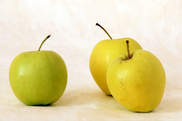 Три желтых яблока на окрашенном фоне — стоковое фото