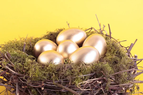 Golden eggs in bird nest over yellow — Stock Photo, Image