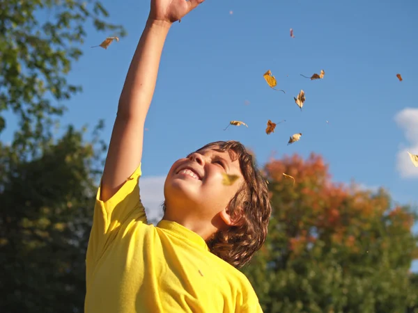 Giovane ragazzo gettando foglie in aria — Foto Stock