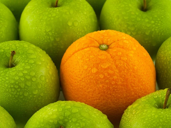 Зеленые яблоки и один апельсин — стоковое фото