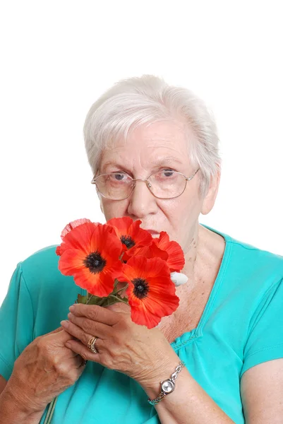 Mujer mayor oliendo amapolas rojas falsas — Foto de Stock