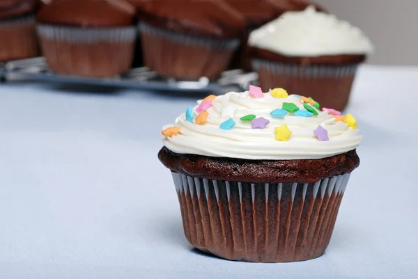 Chocolate cupcake with sprinkles and more in the background — Stock Photo, Image