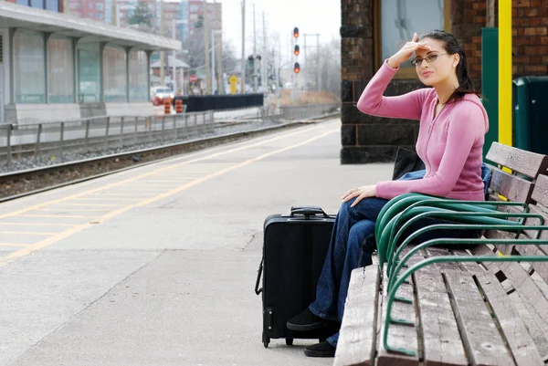 Mulher sentada no banco procurando o trem — Fotografia de Stock