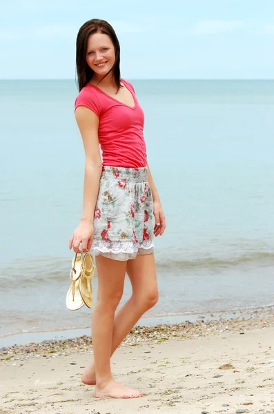Mujer joven sosteniendo sandalias en la playa — Foto de Stock