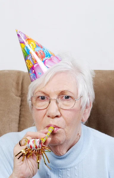 Starší žena s narozeniny klobouk a šum maker — Stock fotografie