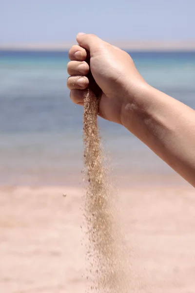 stock image The female hand pours out sand at the seashore