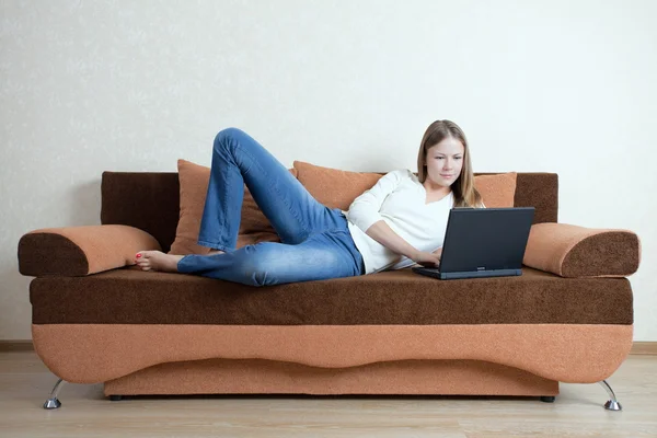 Mujer con portátil en el sofá Imagen de stock