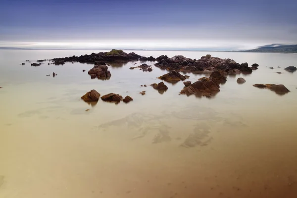 在沙滩上的岩石覆盖着 smoth 平静的海面 — 图库照片