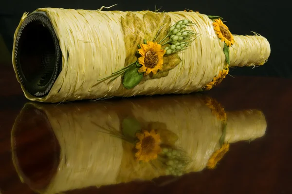 Wijnfles verpakt in gele touw met decoratieve bloemen — Stockfoto