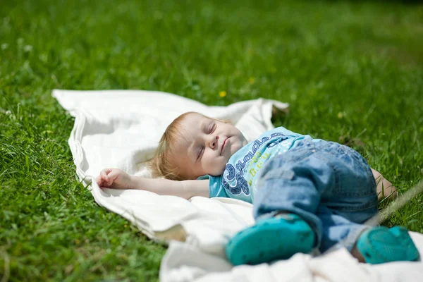 Μικρό αγόρι ύπνο σε μια χλόη για το καλοκαίρι Royalty Free Φωτογραφίες Αρχείου