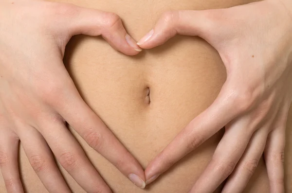Een vrouw handen vormen een hartsymbool rond navel — Stockfoto