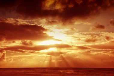 Sunset over sea with moody sky, dark storm clouds, and red light clipart