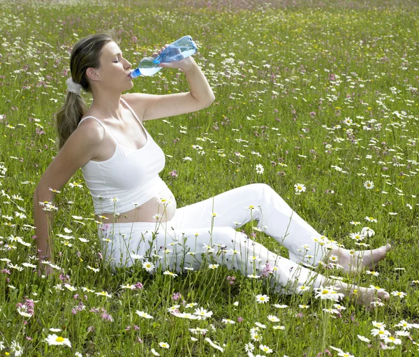 Gravid kvinna på äng med flaska vatten — Stockfoto
