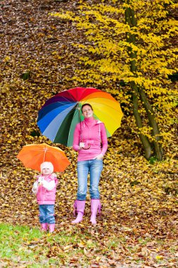 Mother and her daughter with umbrellas in autumnal nature clipart