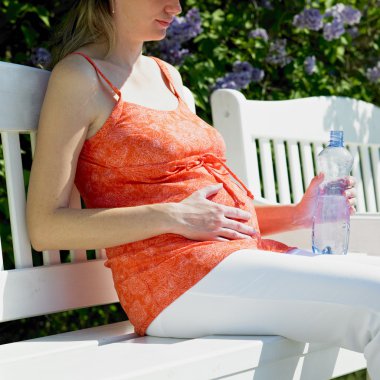 Pregnat woman with bottle of water sitting on bench clipart