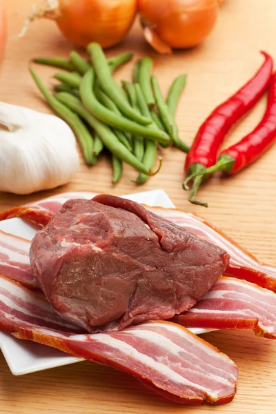 Rauwe vlees en bacon strepen op een houten tafel — Stockfoto