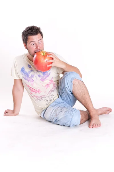 stock image Young man bites a huge tasty apple, on white