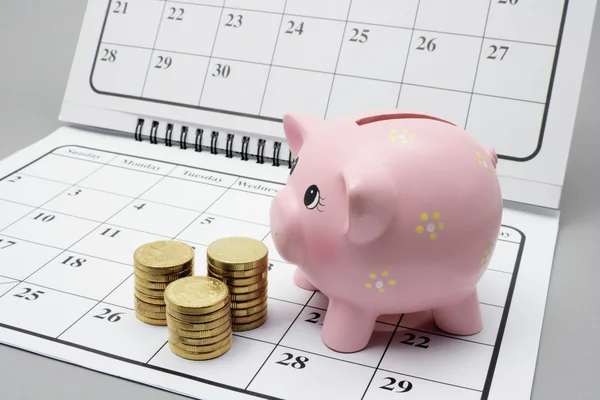 Piggy Bank y monedas en el calendario —  Fotos de Stock