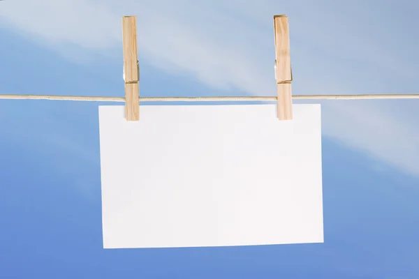 Blanco papier en kleren peg op blauwe hemel — Stockfoto