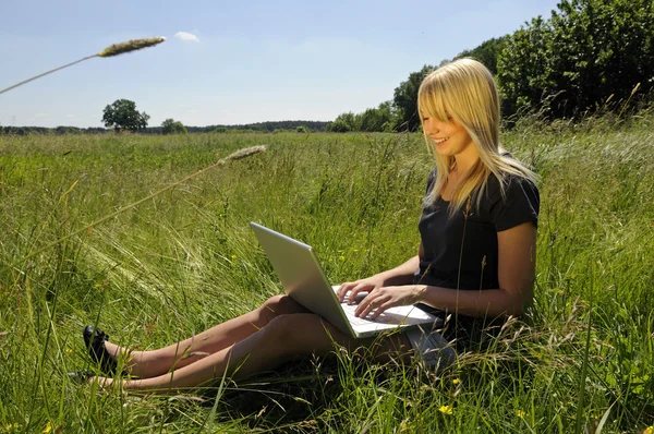 Yong mulher com computador portátil em um prado — Fotografia de Stock