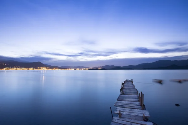 Una romántica puesta de sol azul con un embarcadero sobre un lago con una noche —  Fotos de Stock