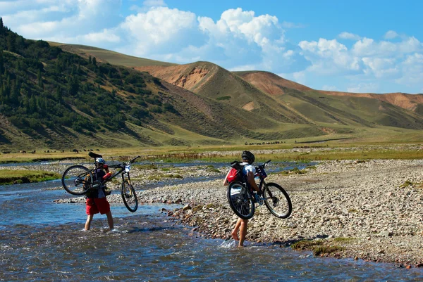 Dois ciclistas de montanha e rio de montanha — Fotografia de Stock