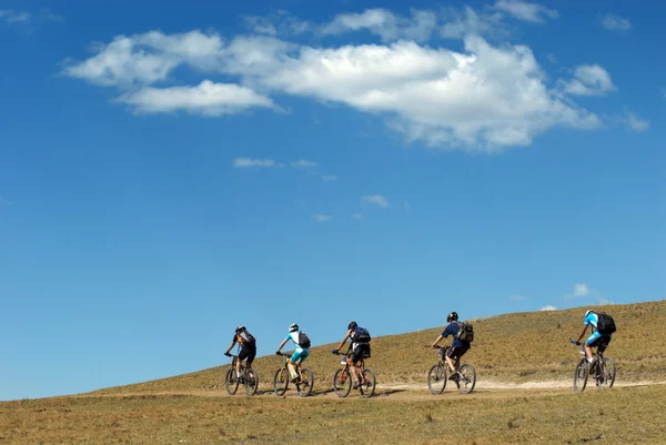 Mountain bikers on rural road and sky — Stock Photo, Image