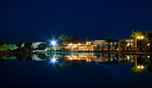 Bar e luzes de um resort tropical refletidos em uma piscina à noite — Fotografia de Stock