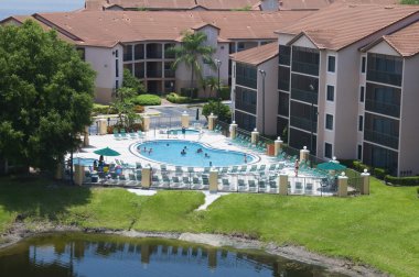 Resort pool near a lake surrounded by condominiums clipart