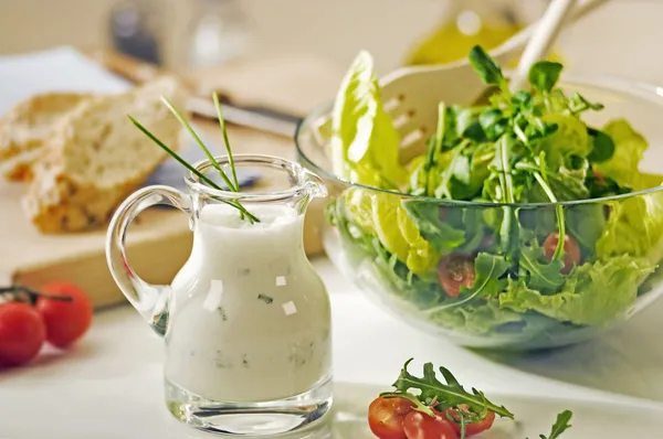 Bowl of greens and a jug of salad dressing — Stock Photo, Image