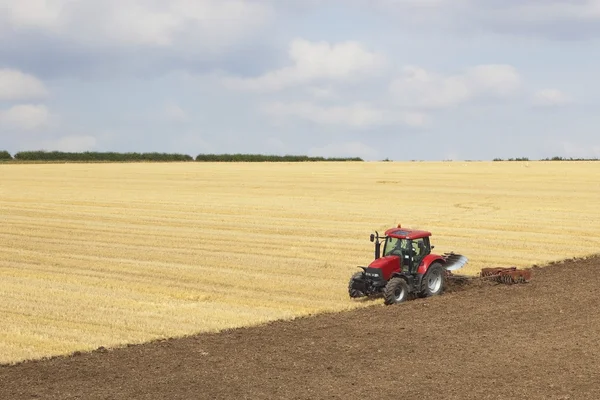 Röd traktor plöjer ett fält — Stockfoto