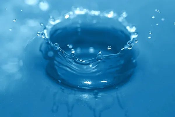 Water drop enters in blue water — Zdjęcie stockowe
