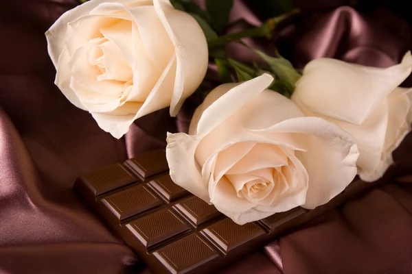 Białe róże na brązowy jedwabiu i czekolada — Zdjęcie stockowe