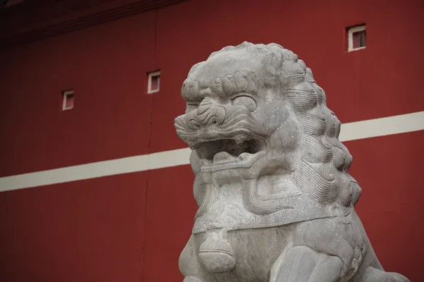 Socha kamenného lva před červenou zeď — Stock fotografie