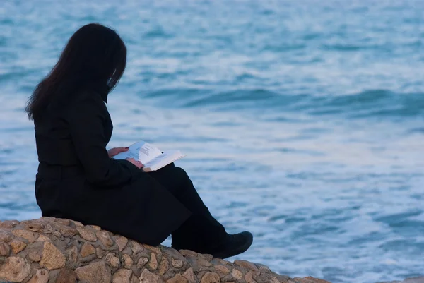 Молодая женщина читает книгу у моря — стоковое фото