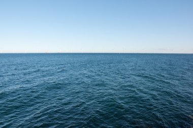 Windmill turbines in a row in the open sea clipart