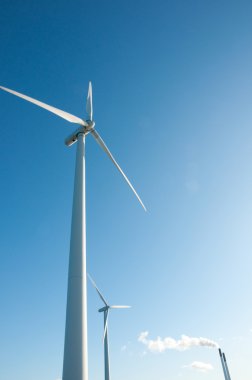 Two windmills and industrial chimney on sunny da clipart