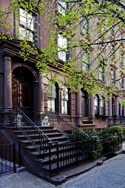 A residential New York, Philadelphia, Boston or Chicago brownstone townhouse building with black fence and steps in front.