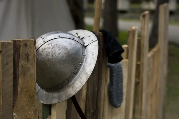 Velho capacete de cavaleiro na cerca com alguns cavaleiros no fundo — Fotografia de Stock