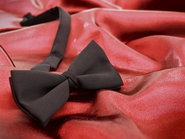 Black bow tie against red satin backgrou — Stock Photo, Image