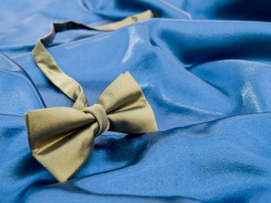 Gold bow tie against blue satin clipart