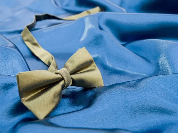 Laço de ouro gravata contra cetim azul — Fotografia de Stock