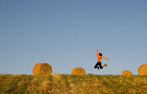 Frau springt in ein Heuballenfeld — Stockfoto