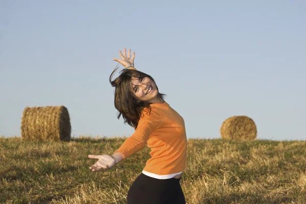 Hermosa mujer abierta es brazos en un campo con fardos de heno — Foto de Stock