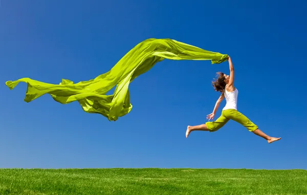 Mulher pulando em um prado verde com um tecido colorido — Fotografia de Stock