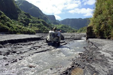 Adventure driving off-road vehicles fording river to mount pinatubo clipart