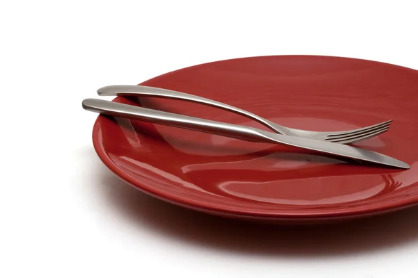 Knife and fork on red shiny plate — Stock Photo, Image