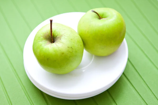 Två gröna äpplen på en vit platta Stockbild